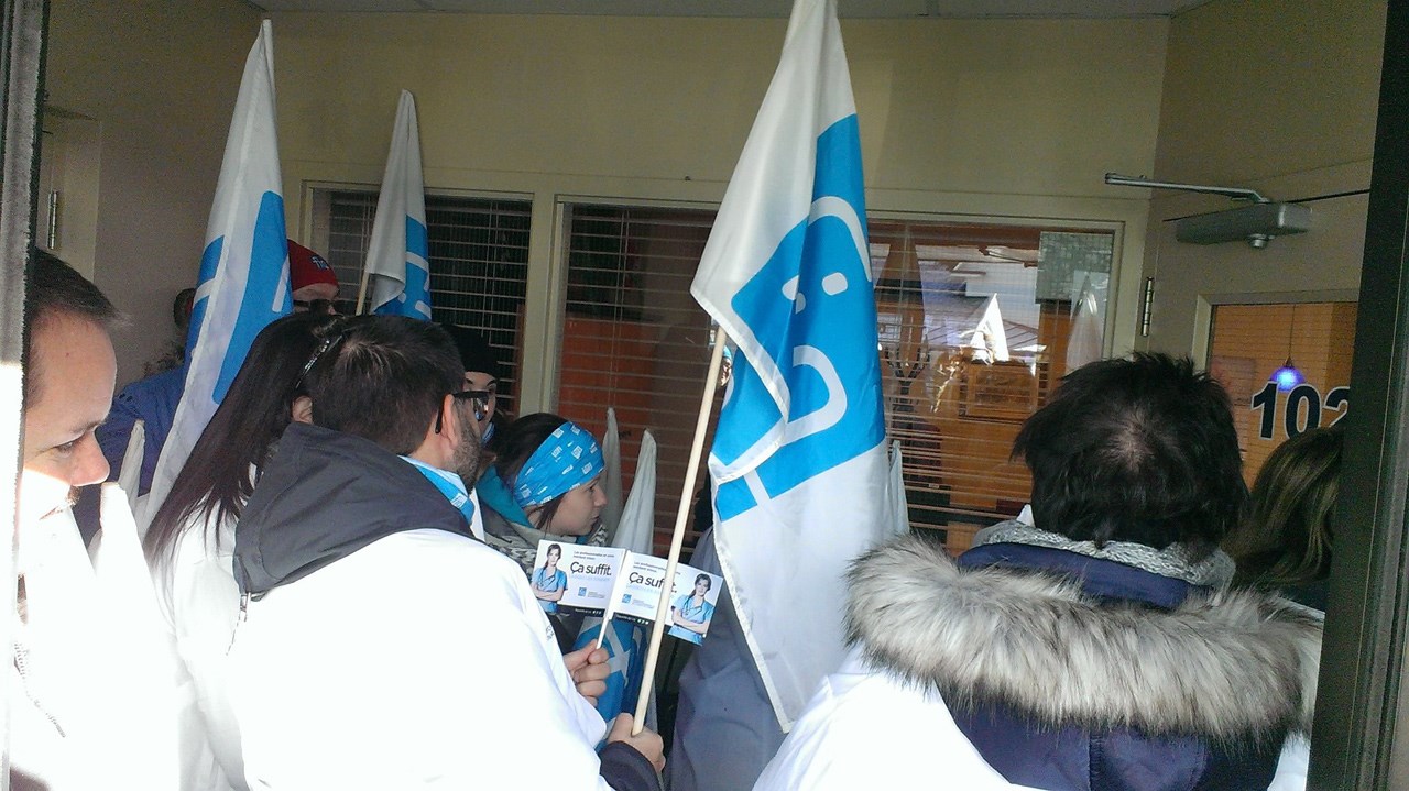 Les manifestants, vêtus de leur sarrau et équipés de drapeau et de pancartes à l’effigie de la FIQ, veulent entrer dans le local de M. Busque.
