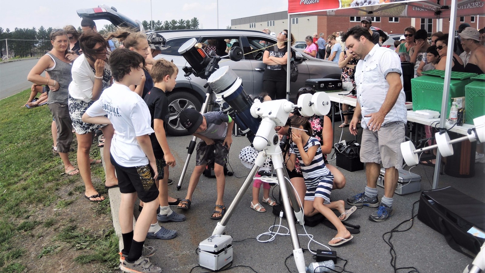 Le vice-président du Club d'astronomie de Saint-Georges, Benoît Bélanger (arborant un T-Shirt blanc à droite de la photo), explique aux gens les différentes composantes de l'éclipse solaire partielle qu'ils aperçoivent dans le télescope.