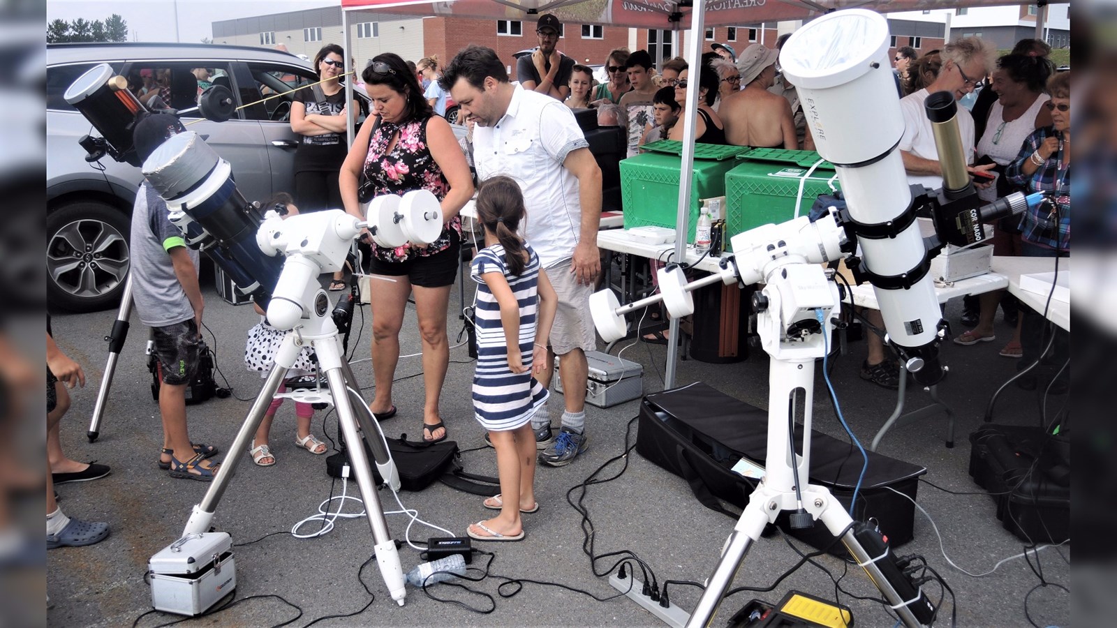 Le vice-président du Club d'astronomie de Saint-Georges, Benoît Bélanger (arborant un T-Shirt blanc), explique aux gens les différentes composantes de l'éclipse solaire partielle qu'ils aperçoivent dans le télescope.