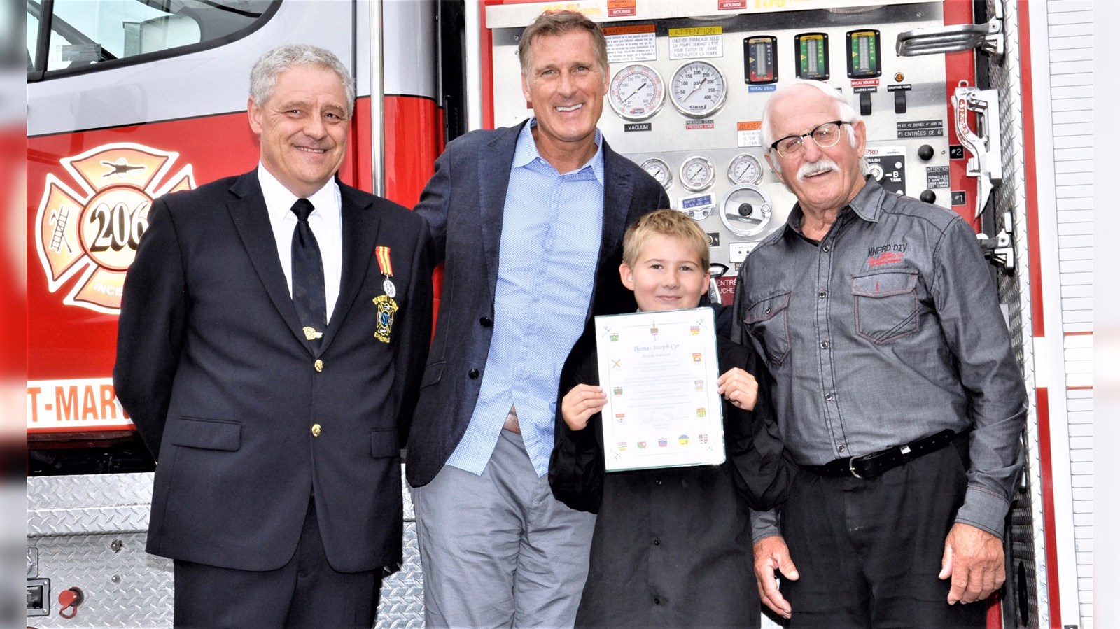 Thomas Joseph Cyr, âgé de 9 ans et originaire de Saint-Martin, reçoit un certificat d'acte de bravoure de la part du député de Beauce, Maxime Bernier. Ils sont entourés du directeur du Service de sécurité incendie de Saint-Martin, Saint-René et Saint-Théophile, Stéphane Maheux, à gauche, et du maire de Saint-Martin, Jean-Marc Paquet, à droite.
