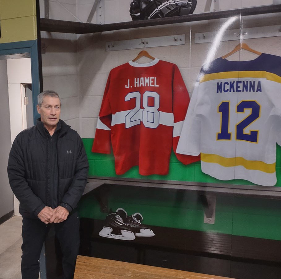 Jean Hamel posant près de la reproduction de son chandail aux couleurs rappelant celles des Canadiens de Montréal