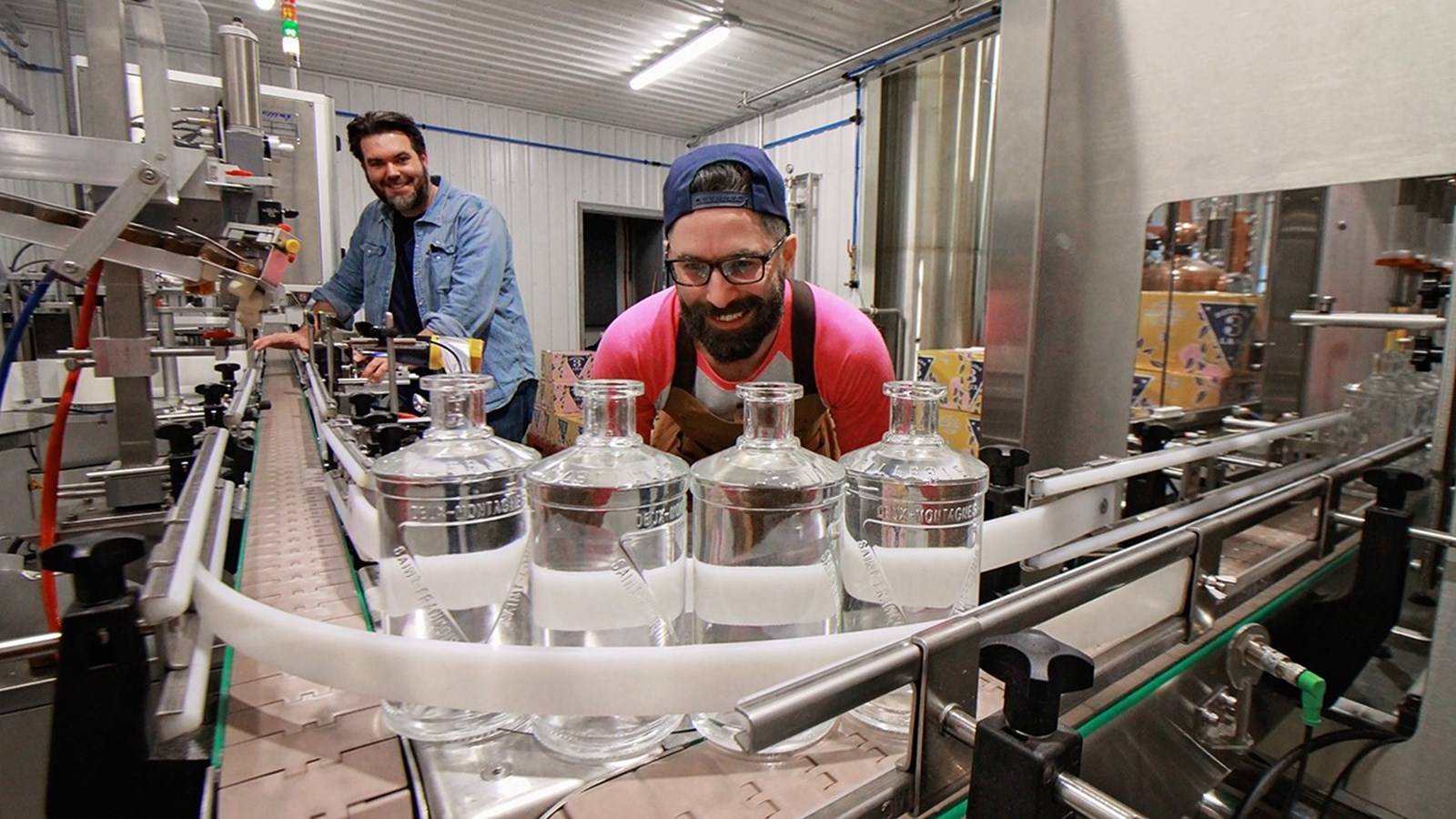 Dominic Proulx, chef distillateur et copropriétaire de la Distillerie 3 Lacs et Mathieu Caron, copropriétaires de l’entreprise pose devant la nouvelle chaîne d'embouteillage automatisée