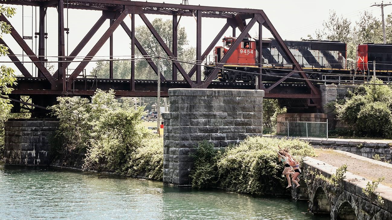 Trois adolescentes sautent à l'eau en pleine canicule alors que le train du Canadien national passe au-dessus du canal Soulages à Les Coteaux. 