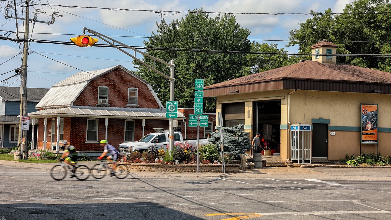 Deux cyclistes traversant la municipalité de Saint-Clet à l'angle de la route 201 et du boulevard de la Cité-des-Jeunes.