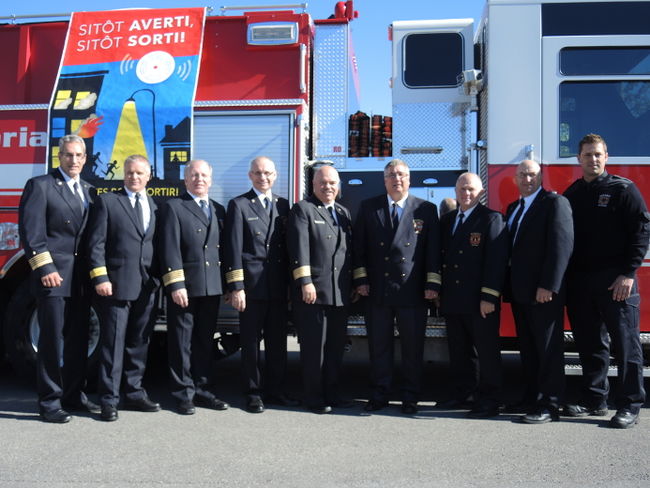 Les neuf Directeurs des services d'incendie de l'Entraide intermunicipale posant devant l'affiche officielle.