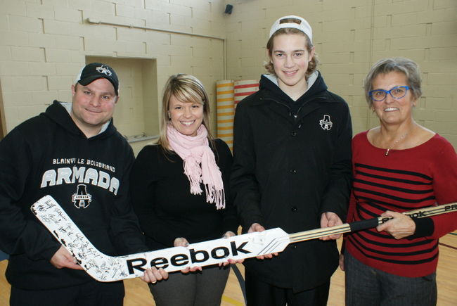 L’entraîneur de l’Armada, Jean-François Houle, Katrine Pilon du PREL, Samuel Montembeault, gardien de but, ainsi que Jocelyne Cloutier, représentante de la Ville de Mont-Laurier, tiennent dans les mains un bâton de hockey autographié. 