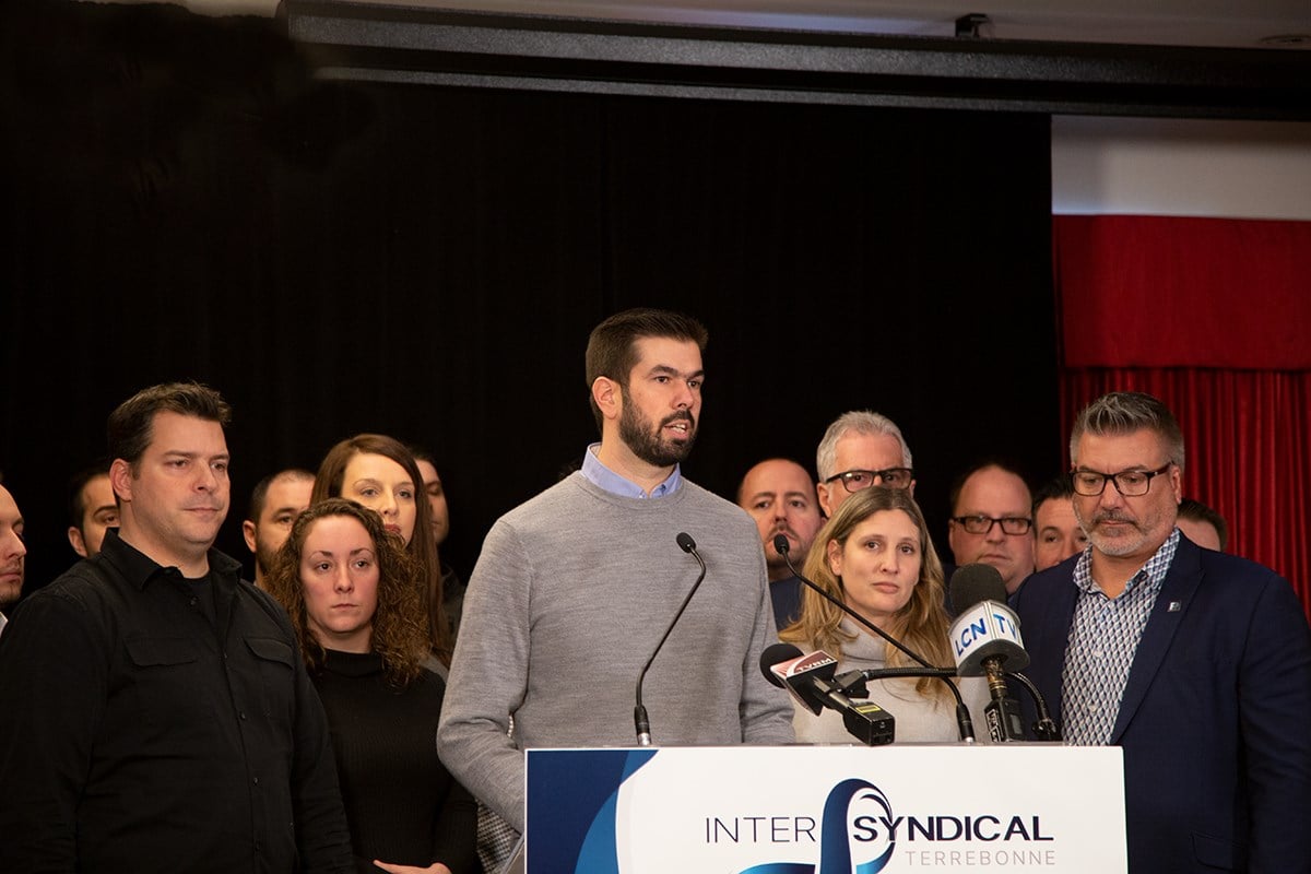 Au micro, Guillaume Tremblay, président du Syndicat des employés manuels de Terrebonne, avec à sa gauche Sylvain Roy, président du Syndicat des pompiers de la Rive-Nord et à sa droite, Chantal Riopel, présidente du Syndicat des cols blancs et Patrick Lepage, président de la Fraternité des policiers de Terrebonne, entourés de collègues et des membres des divers exécutifs syndicaux.